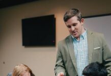 
			
				                                Assistant Dean of the Tillman School of Business Waylon Woodall (standing) supervises students with the VITA tax preparation process. (UMO photo)
 
			
		