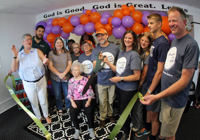 131570729_web1_Ribbon-falls-2
Brad Mitchell and Jennifer Bland use a large pair of ceremonial scissors Friday afternoon for the ribbon-cutting ceremony for the Mount Olive location of their Grounded and Baked bakery and coffee shop. The bakery features baked goods using the recipes Mitchells grandmother, Norma Ann Nanny Vinson, seated, taught him. From left are, Mount Olive Area Chamber of Commerce President Julie Beck; Chamber board Chairman Edward Olive; Mitchells wife, Wendy; Mount Olive town Commissioner Vicky Darden; Mitchells aunt, Debbie Hardy; Norma Ann Nanny Vinson; Mitchells mother, Dianne Mitchell; Chamber Ambassador Pernell Brickey; Mitchell; Bland and her daughter, Collins; son, Andrew; and husband Frank. The business is located in the old Henderson-Crumpler Clinic, 229 N. Center St. (Steve Herring|mountolivetribune.com)